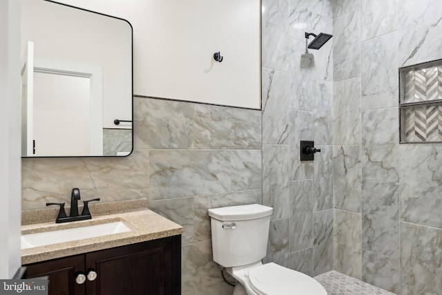 bathroom with toilet, a tile shower, tile walls, and vanity