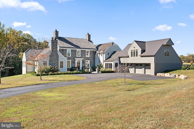 view of front of property with a front lawn, aphalt driveway, metal roof, a chimney, and a standing seam roof