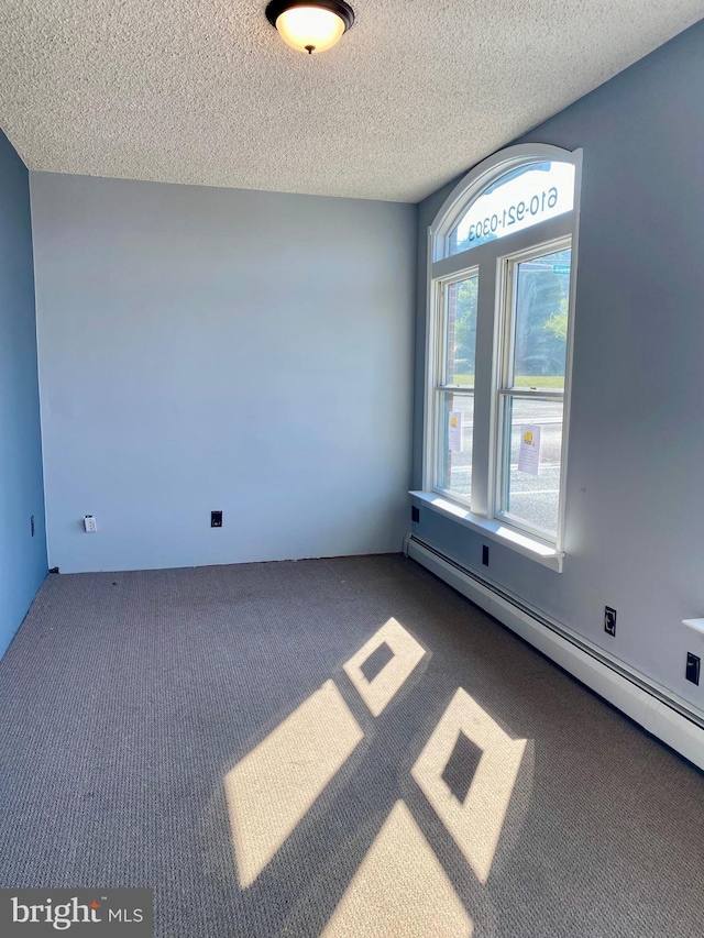 carpeted spare room with a baseboard heating unit and a textured ceiling