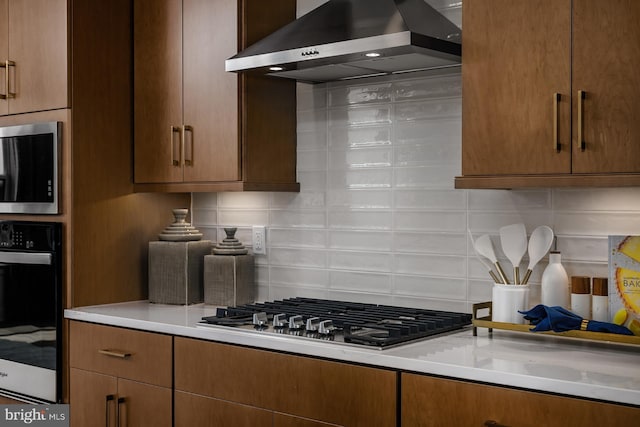 kitchen with wall chimney range hood, stainless steel appliances, and tasteful backsplash