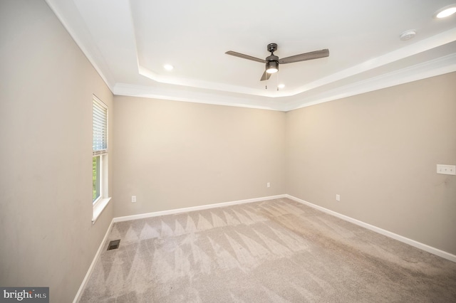 empty room with ceiling fan, crown molding, light carpet, and a raised ceiling