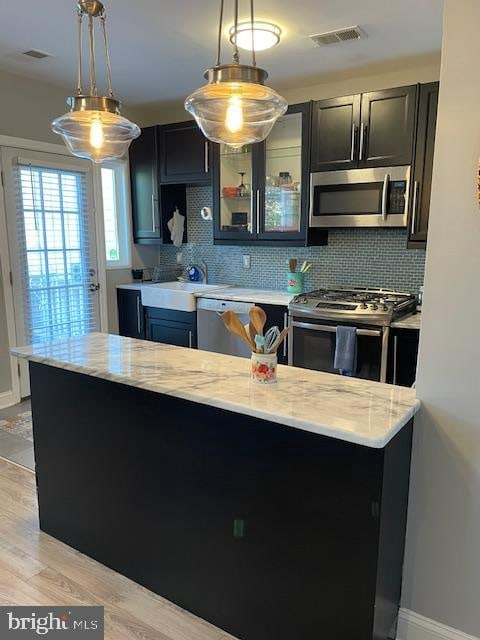 kitchen with stainless steel appliances, hanging light fixtures, backsplash, and light wood-type flooring