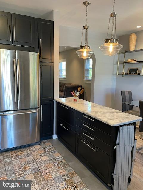 kitchen with light stone counters, kitchen peninsula, decorative light fixtures, light hardwood / wood-style flooring, and stainless steel refrigerator