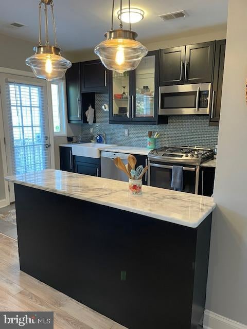 kitchen with stainless steel appliances, decorative backsplash, decorative light fixtures, and light hardwood / wood-style flooring