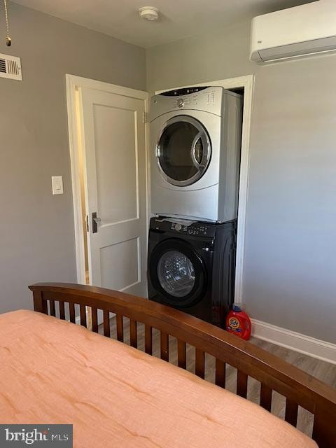 clothes washing area featuring a wall unit AC, stacked washer / drying machine, and wood-type flooring