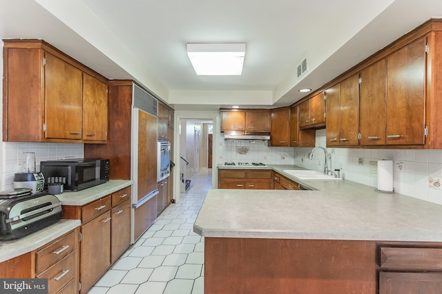 kitchen with paneled built in fridge, kitchen peninsula, decorative backsplash, sink, and oven