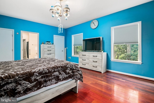 bedroom with a notable chandelier, ensuite bathroom, and dark hardwood / wood-style flooring