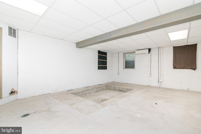 basement featuring a drop ceiling and a wall mounted air conditioner