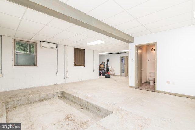 basement featuring a drop ceiling and a wall mounted air conditioner