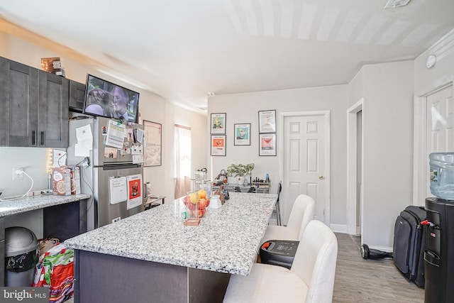 kitchen featuring freestanding refrigerator, a kitchen breakfast bar, light wood-style flooring, a kitchen island, and light stone counters