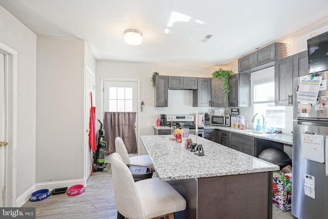 kitchen featuring a breakfast bar, a kitchen island, a sink, stainless steel appliances, and baseboards