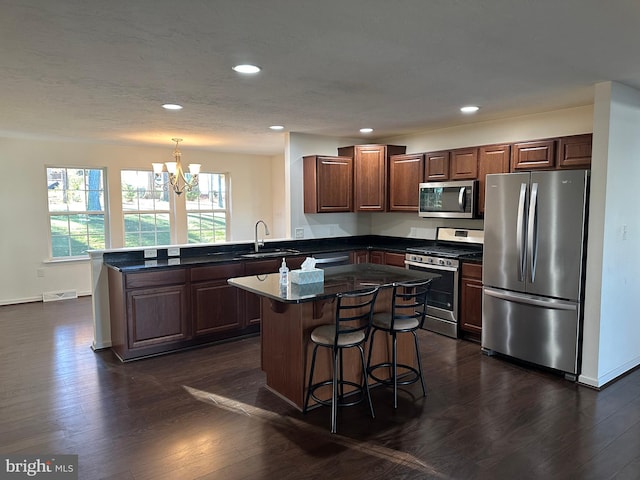 kitchen with dark wood-type flooring, kitchen peninsula, stainless steel appliances, pendant lighting, and an inviting chandelier