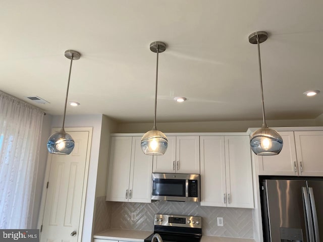 kitchen with white cabinets, decorative backsplash, stainless steel appliances, and hanging light fixtures