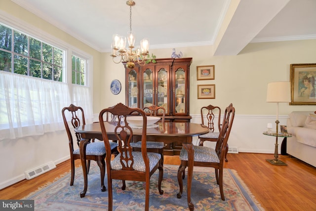 dining area featuring wood-type flooring, ornamental molding, and an inviting chandelier