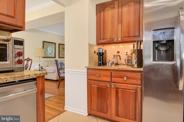 kitchen featuring light stone counters, ornamental molding, light hardwood / wood-style floors, and appliances with stainless steel finishes