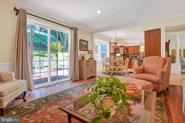 living room with light wood-type flooring, decorative columns, an inviting chandelier, and ornamental molding