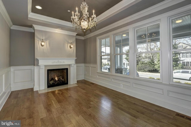 unfurnished living room with wood-type flooring, ornamental molding, a tray ceiling, and an inviting chandelier