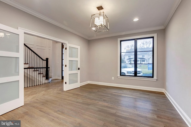 spare room with wood finished floors, a chandelier, ornamental molding, stairs, and baseboards