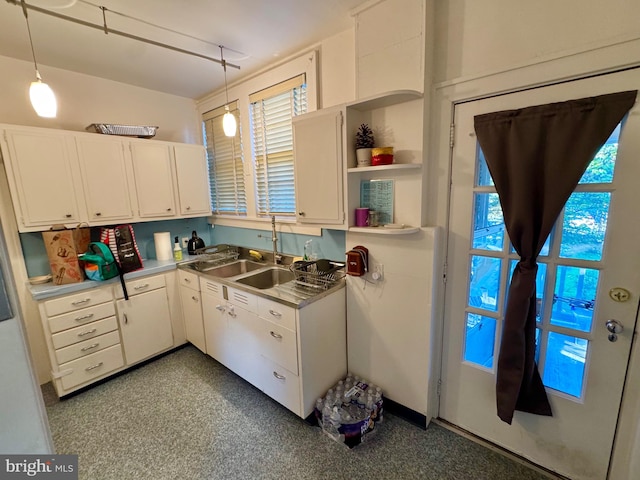 kitchen featuring hanging light fixtures, sink, stainless steel counters, and white cabinetry