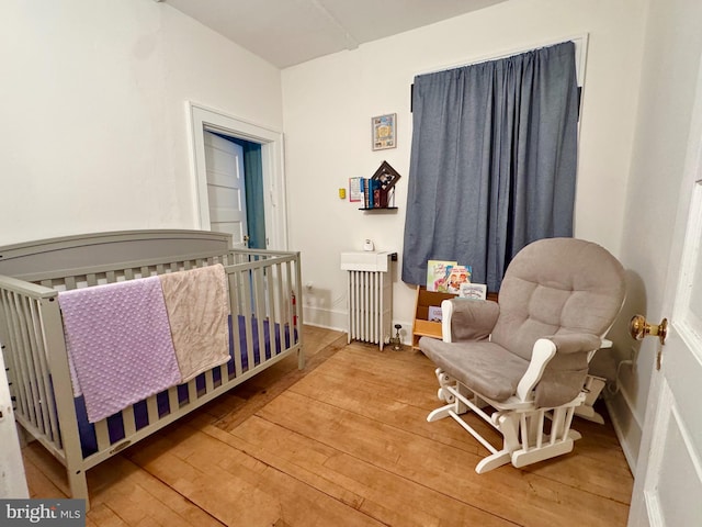 bedroom featuring a nursery area, radiator, and wood-type flooring