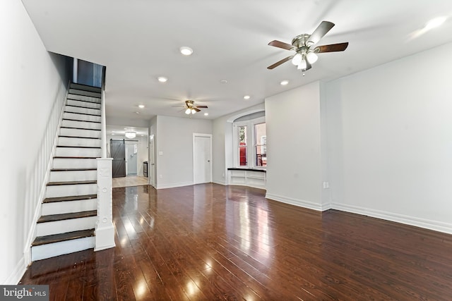 unfurnished living room featuring a barn door, ceiling fan, and dark wood-type flooring