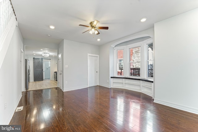 unfurnished room featuring wood-type flooring, a barn door, and ceiling fan