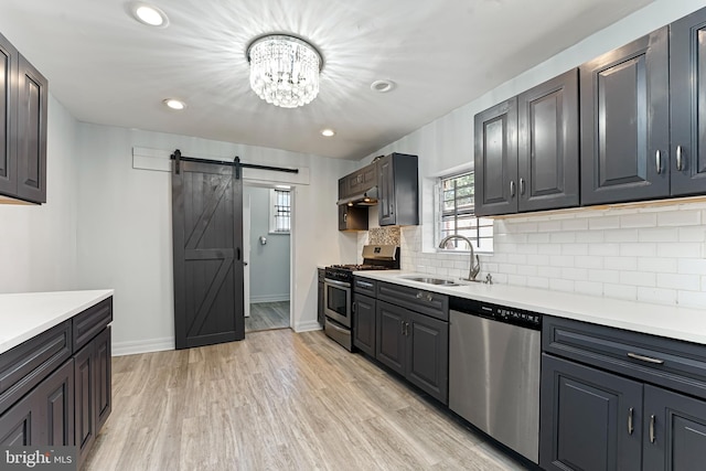 kitchen with sink, light hardwood / wood-style flooring, appliances with stainless steel finishes, a notable chandelier, and a barn door