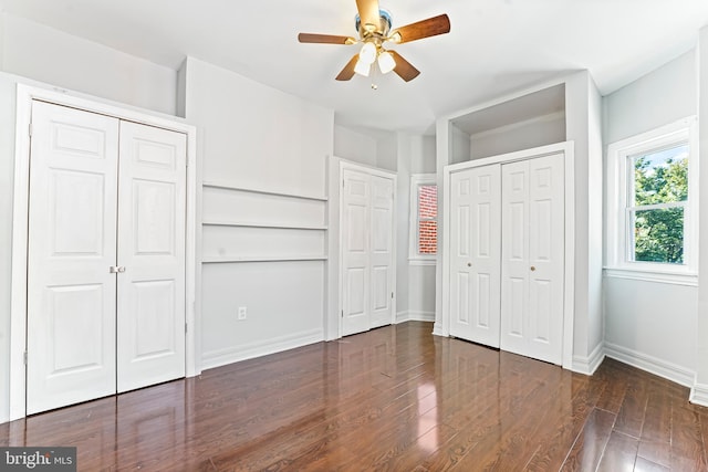 unfurnished bedroom with ceiling fan, two closets, and dark wood-type flooring