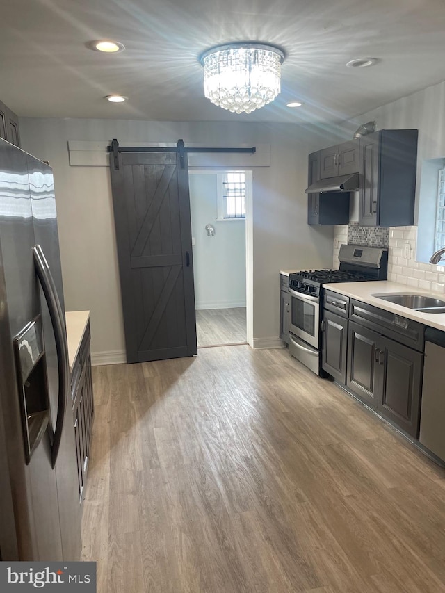 kitchen featuring stainless steel appliances, light hardwood / wood-style floors, a barn door, and sink