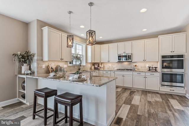 kitchen with light stone counters, a peninsula, white cabinetry, hanging light fixtures, and appliances with stainless steel finishes