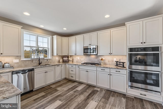 kitchen with appliances with stainless steel finishes, dark wood finished floors, a sink, and backsplash