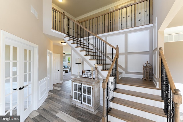 staircase featuring french doors, visible vents, a decorative wall, a high ceiling, and wood finished floors