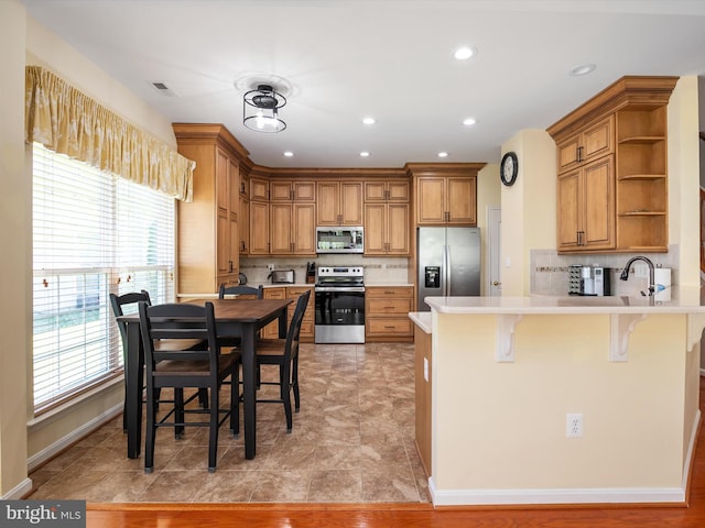 kitchen featuring kitchen peninsula, a kitchen bar, stainless steel appliances, light hardwood / wood-style floors, and decorative backsplash