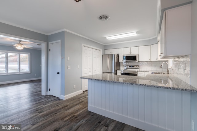 kitchen featuring white cabinets, appliances with stainless steel finishes, light stone countertops, dark hardwood / wood-style floors, and ornamental molding