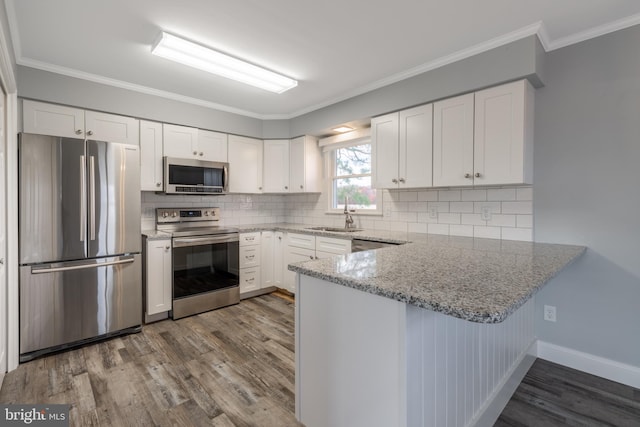 kitchen with wood-type flooring, white cabinetry, stainless steel appliances, light stone counters, and ornamental molding