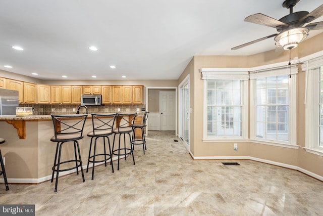 kitchen featuring sink, a kitchen bar, tasteful backsplash, light stone counters, and ceiling fan