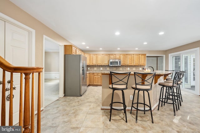 kitchen with decorative backsplash, appliances with stainless steel finishes, a center island with sink, and a kitchen breakfast bar