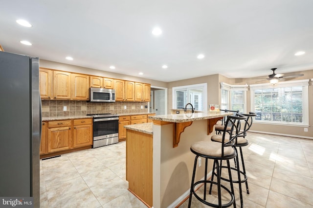 kitchen with tasteful backsplash, light stone countertops, stainless steel appliances, a breakfast bar area, and a center island with sink