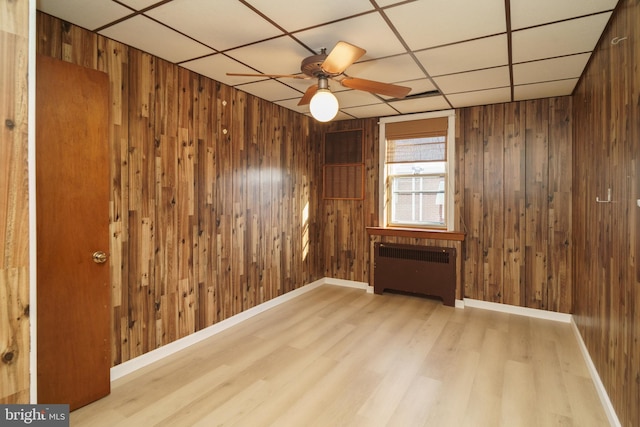 spare room featuring wooden walls, ceiling fan, radiator, and light hardwood / wood-style flooring