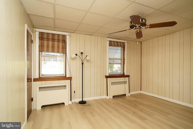 empty room with radiator, ceiling fan, a drop ceiling, and light hardwood / wood-style floors