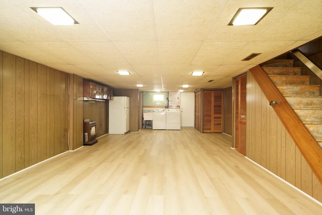 basement with white fridge, light wood-type flooring, separate washer and dryer, and wooden walls