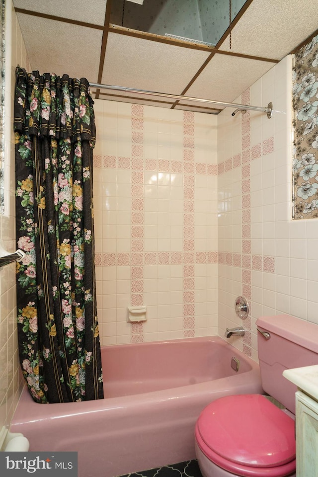 bathroom with a drop ceiling, shower / tub combo with curtain, and toilet