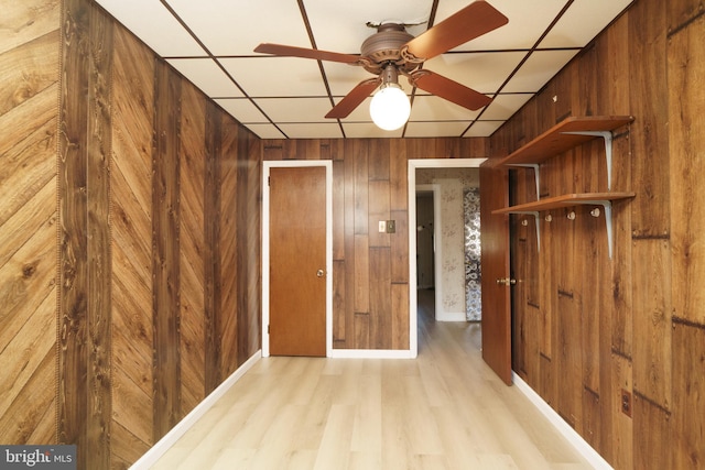 hallway featuring a paneled ceiling, light hardwood / wood-style floors, and wooden walls