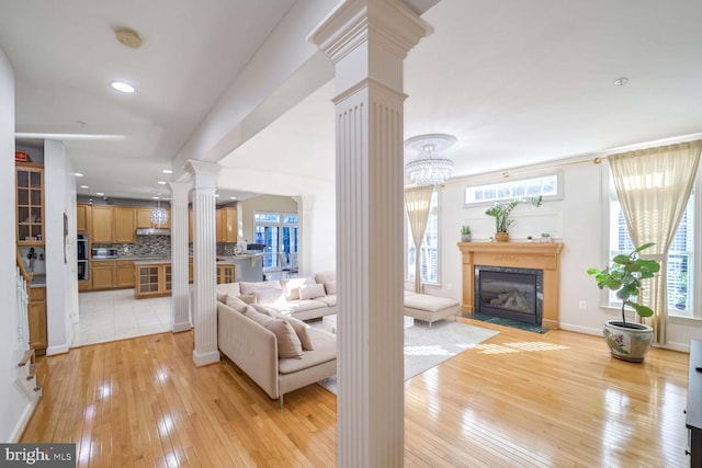 living room featuring decorative columns, light wood-type flooring, a healthy amount of sunlight, and a chandelier