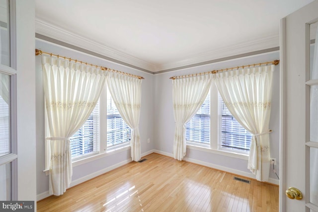 empty room featuring plenty of natural light, crown molding, and light hardwood / wood-style flooring