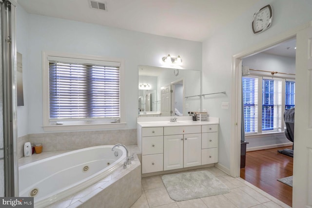 bathroom featuring tile patterned flooring, vanity, and a relaxing tiled tub