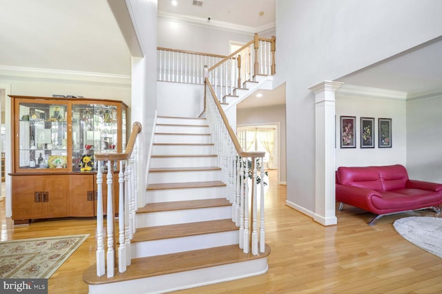 stairs featuring hardwood / wood-style flooring, ornate columns, and ornamental molding