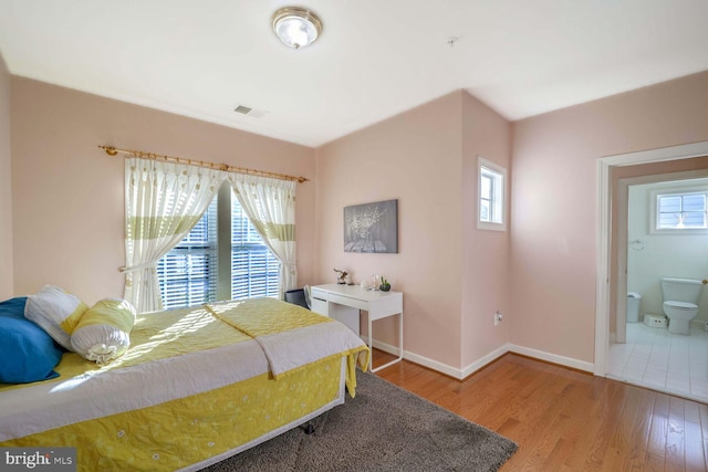 bedroom featuring ensuite bath, wood-type flooring, and multiple windows