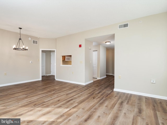 empty room with an AC wall unit, light hardwood / wood-style flooring, and a notable chandelier