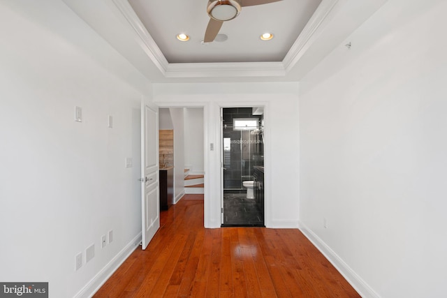 hall with hardwood / wood-style flooring, crown molding, and a raised ceiling